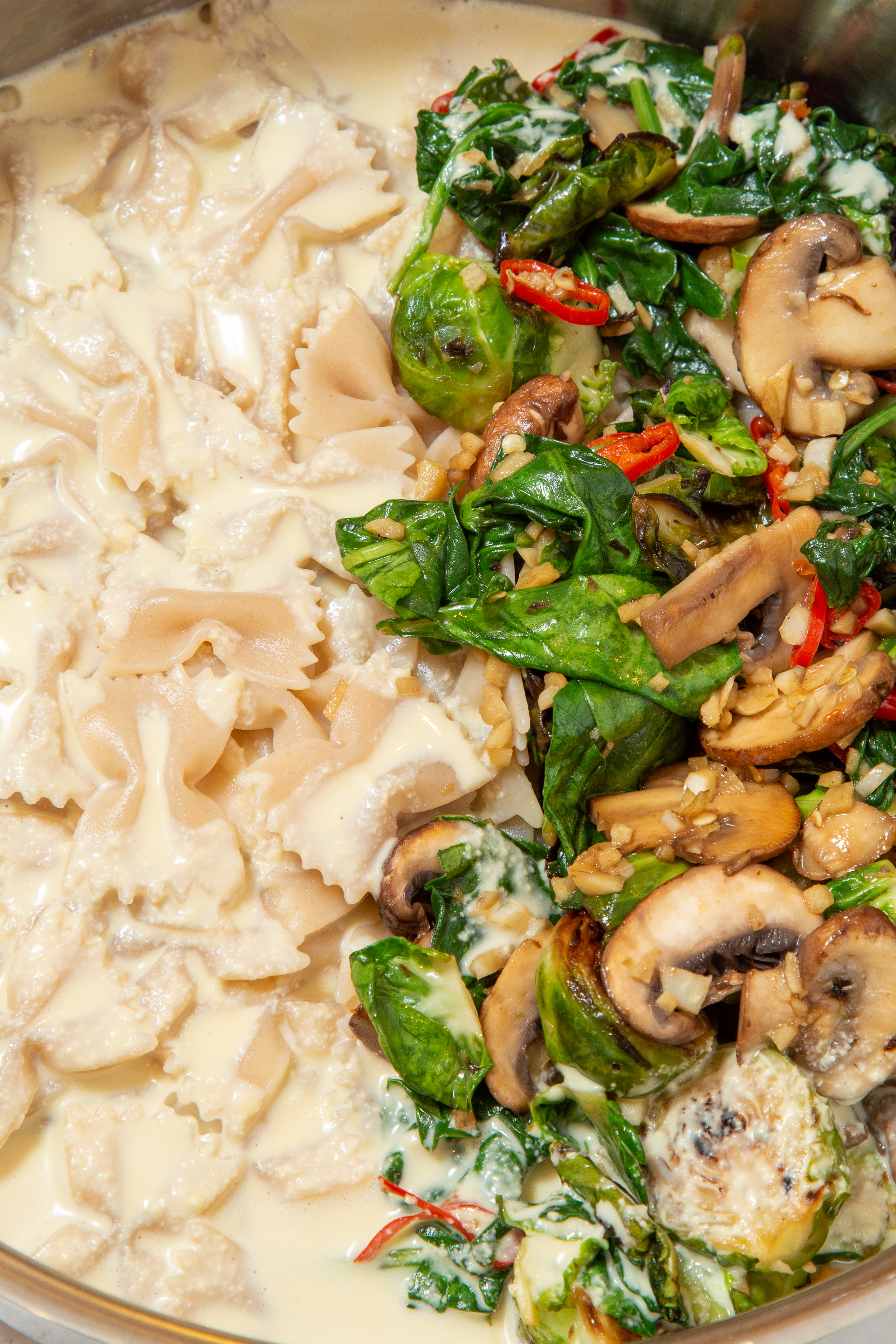 Sautéed vegetables next to creamy pasta in pot